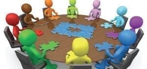 Colorful figures sit around a table with puzzle pieces scattered on the surface.