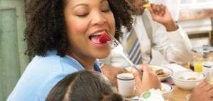 Woman eating a strawberry while sitting at a table with others.