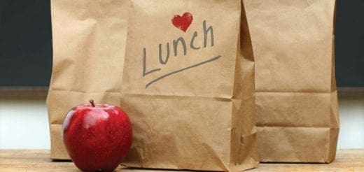 Brown paper lunch bags with "Lunch" written on one, and a red apple in front.