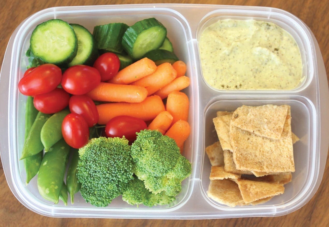 Bento box lunch with vegetables, hummus, and crackers.