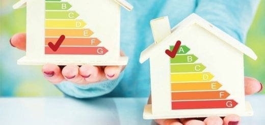 Two house models with energy efficiency labels are held by hands.