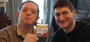 Two men smile for the camera, one holding a small box.