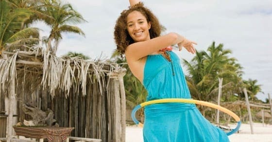 Woman in a blue dress hooping on a beach.
