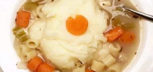 Bowl of chicken noodle soup topped with a scoop of mashed potatoes and a carrot slice.