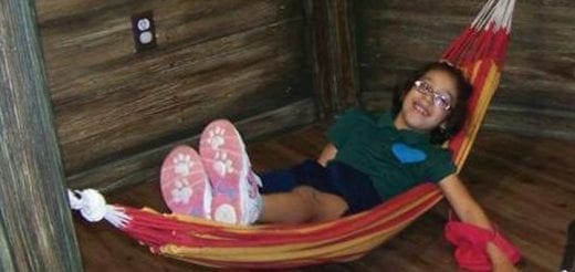 Child with glasses smiles while lying in a colorful hammock.