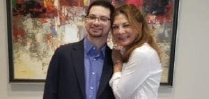 A man and woman smile in front of an abstract painting.