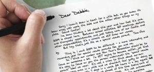 Hand writing "Dear Debbie," on a letter with a black pen.