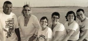Six people pose for a photo on a beach.