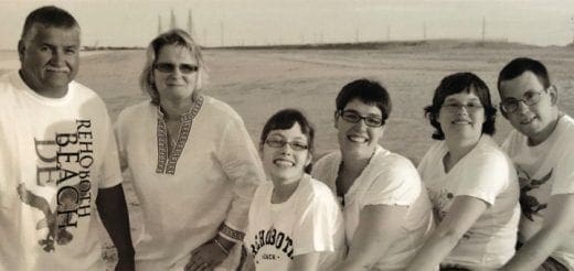 Six people pose for a photo on a beach.