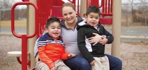 A mother smiles with her two young sons on a playground.