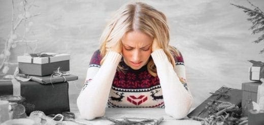 Woman with hands on head, surrounded by holiday gifts, looking distressed.