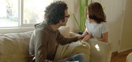 Two people sit on a couch, talking with one person's hand on the other's arm.