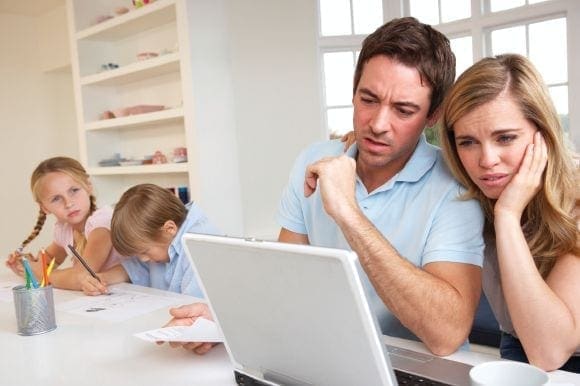 Parents looking stressed at a laptop while two children do schoolwork