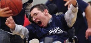 Man in a wheelchair playing basketball with arms raised and mouth open