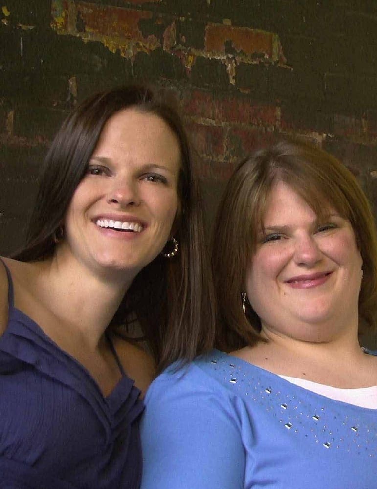 Angela Ruzicka and Amanda Angela smiling in front of a brick wall.