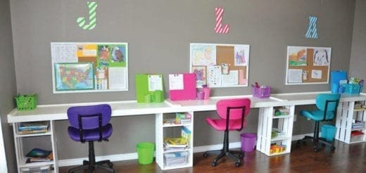 A long white desk with three workstations, each with a colorful chair, organized with bins and corkboards on the wall.