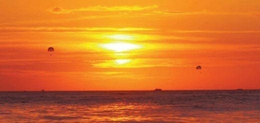 Sunset over the ocean with two parasailers and a distant boat