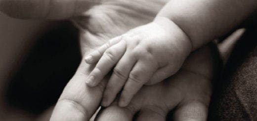 Small infant hand resting gently on an adult palm.