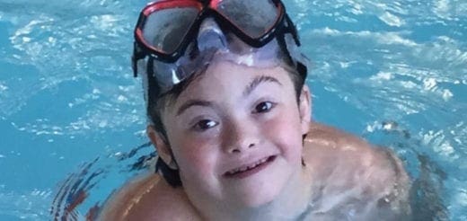 Eli smiles in a swimming pool wearing goggles.