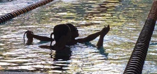 Two swimmers in a pool, with one holding a kickboard.