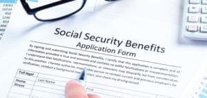 Social Security Benefits Application Form with a hand holding a pen.