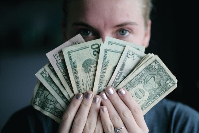Hands holding US dollar bills in front of a person's face.