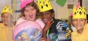 Children wearing paper crowns and party hats smile for the camera.