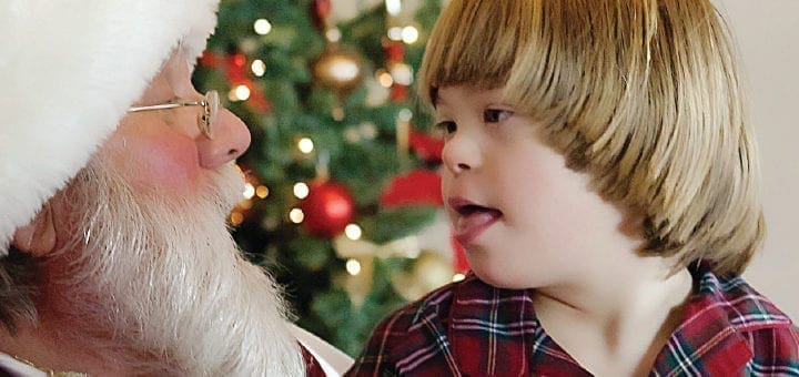 Landyn looking at Santa with a Christmas tree in the background.