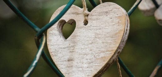 Wooden heart with a carved heart cutout hangs on a fence.