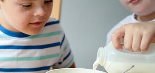 Two children pour milk into a bowl for breakfast.