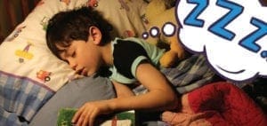 A young boy sleeps in bed with a thought bubble containing "zzz.