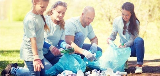 Family picking up trash in a park, placing it in blue garbage bags.