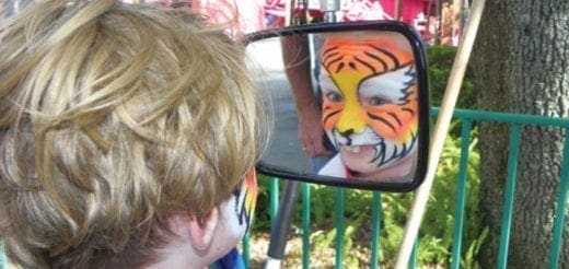 Child with tiger face paint looks in a mirror at their reflection.