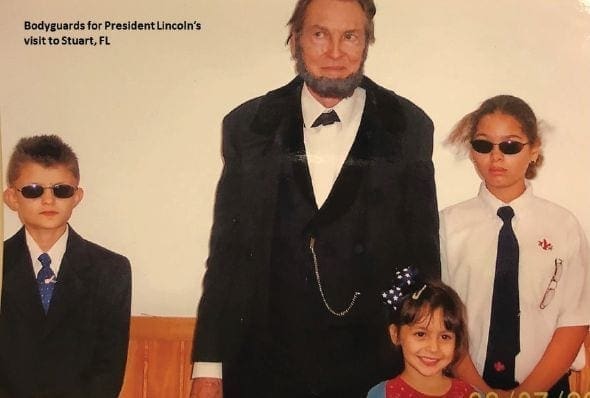 Three people, one adult dressed as Abraham Lincoln and two children, pose for a photo.