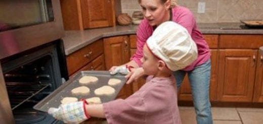 A woman helps a child place a baking sheet of heart-shaped cookies into an oven.