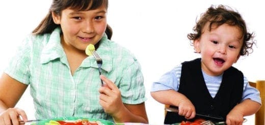 Two children are sitting at a table with food.