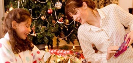 A young girl and a woman in pajamas look at presents under a Christmas tree.