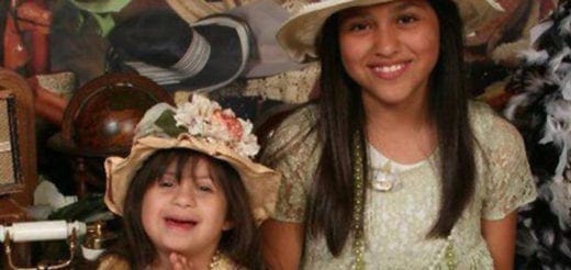 Two young girls wearing bonnets smile in front of a collection of hats.