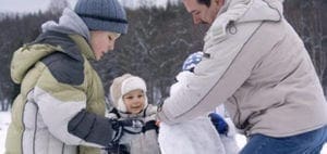 A family builds a snowman in the snow.