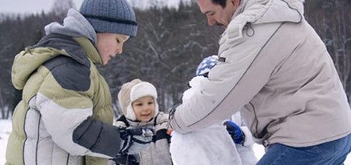 A family builds a snowman in the snow.