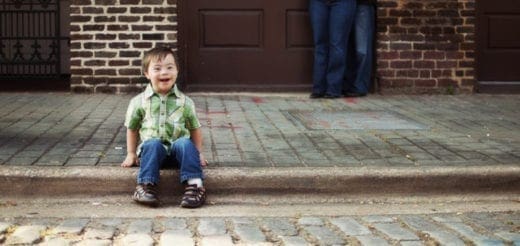A young child sits on steps in front of a brown door and brick wall.