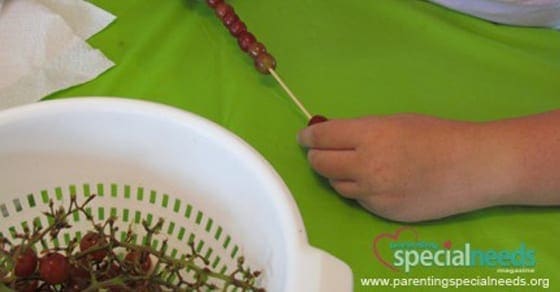 Child threading grapes onto a skewer over a green surface.