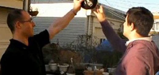 Two men hold up weights outdoors.