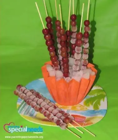 Frozen grapes on sticks arranged in an orange cup on a plate.
