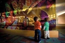 Two children look at a colorful butterfly mural.