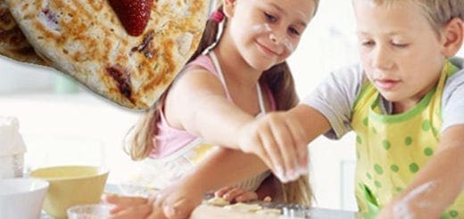 Two children are preparing pancakes with strawberries.