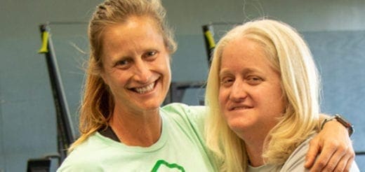 Two women smiling together with their arms around each other in a gym.