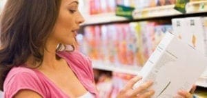 Woman in pink shirt reads label on food box in grocery aisle.