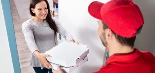 Woman receiving a pizza delivery from a man in a red cap and shirt
