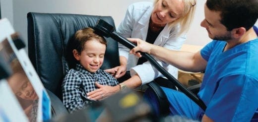 A boy in a chair receives a treatment from two adults.